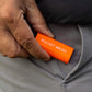 An orange Pocket Brush is being held next to a grey pant pocket.