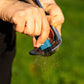 A navy blue Pocket Brush is using the nylon bristles to remove the dirt from the face of a golf club. Debris flies towards the camera.