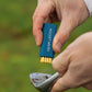 A navy blue Pocket Brush is being held above a dirty golf club with the brass bristles exposed. 