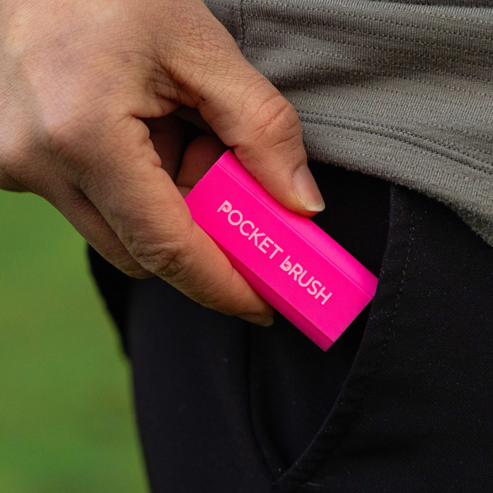 A bright pink Pocket Brush is being inserted into a black pants pocket