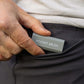 A grey Pocket Brush is being held next to a black pant pocket