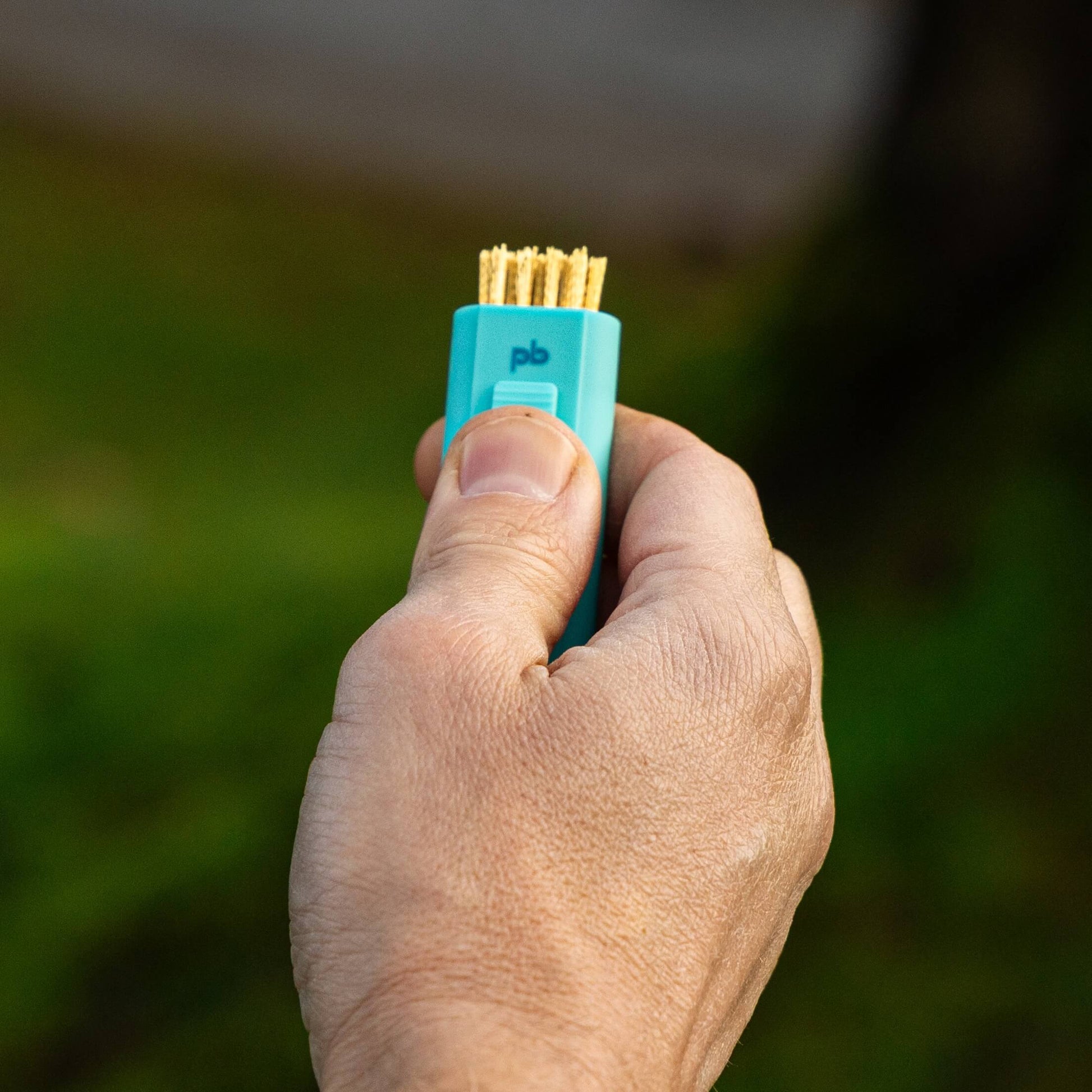 A light blue Pocket Brush is being held up with the brass bristles exposed