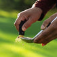 A black Pocket Brush is using its brass bristles to remove the dirt from a dirty golf club face.