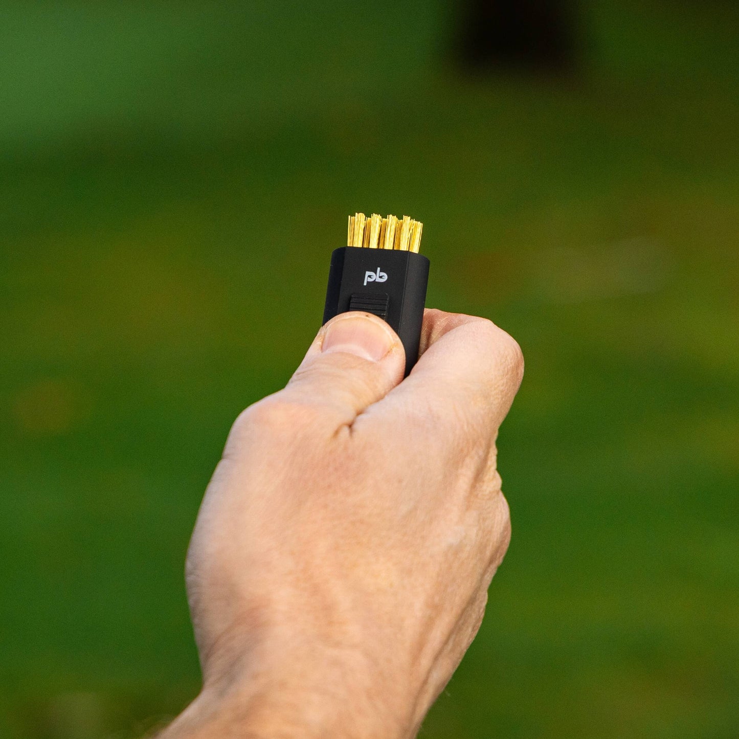 A black pocket brush is being held with its brass bristles exposed