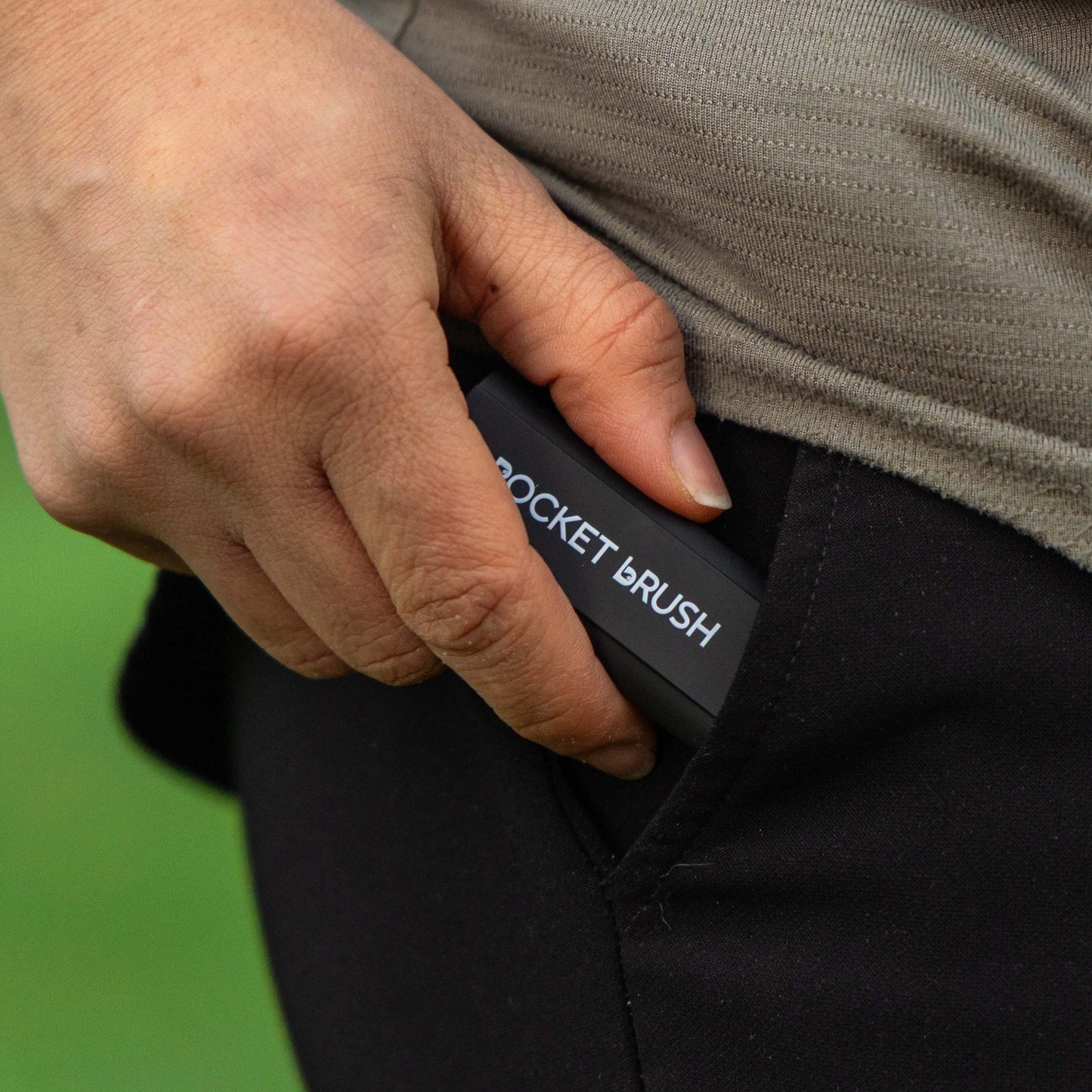 A black pocket brush is being inserted into a black pants pocket