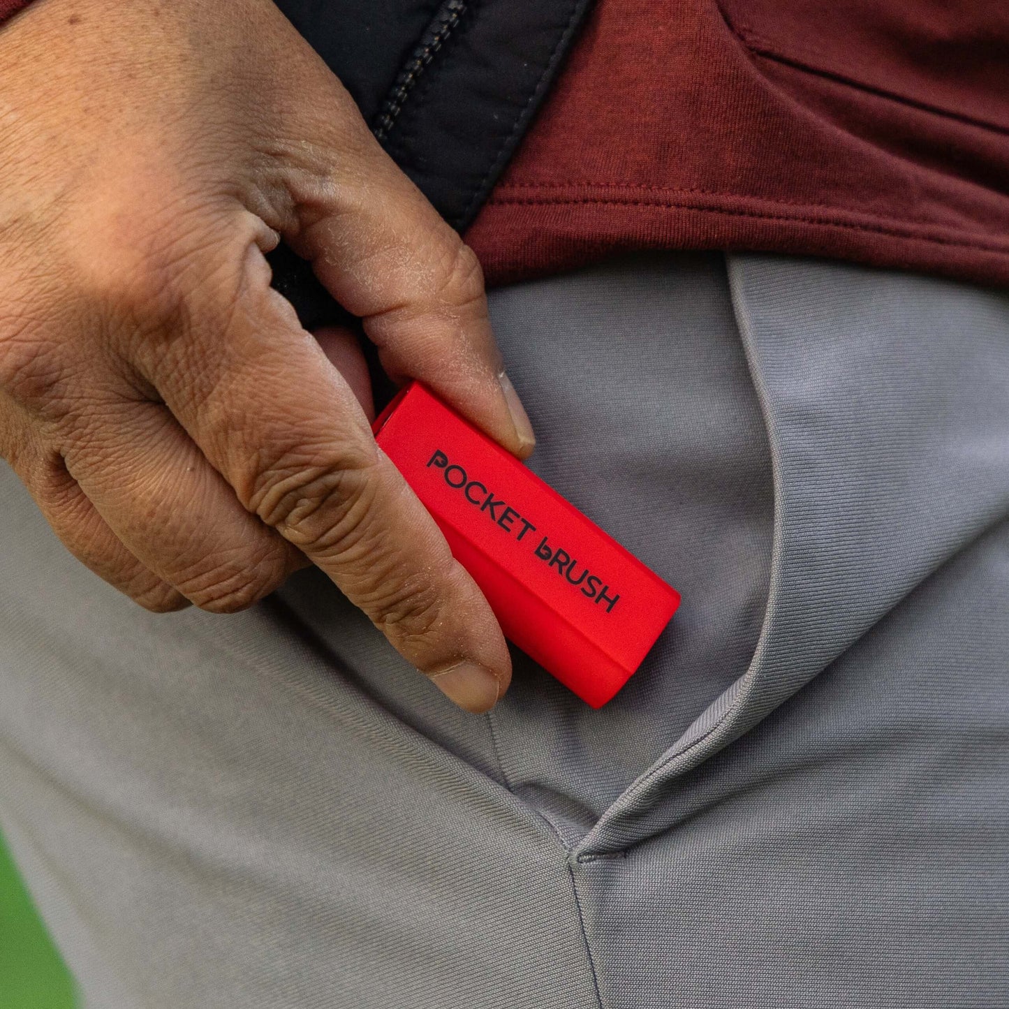 A red Pocket Brush is being held next to a grey pant pocket.
