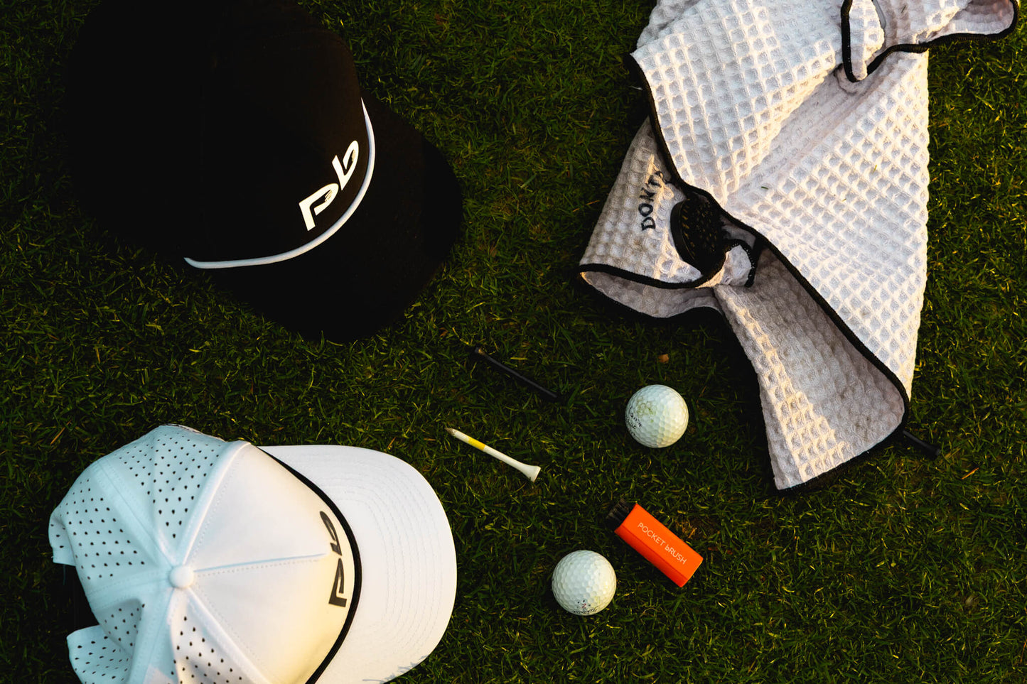 Golf accessories including a pocket brush cap, towel, golf balls, and club on grass