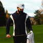 Man with a white pocket brush hat on a golf course holding a golf club with a blurred autumn background