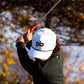 Person playing golf with a white pocket brush cap featuring a logo in an outdoor setting