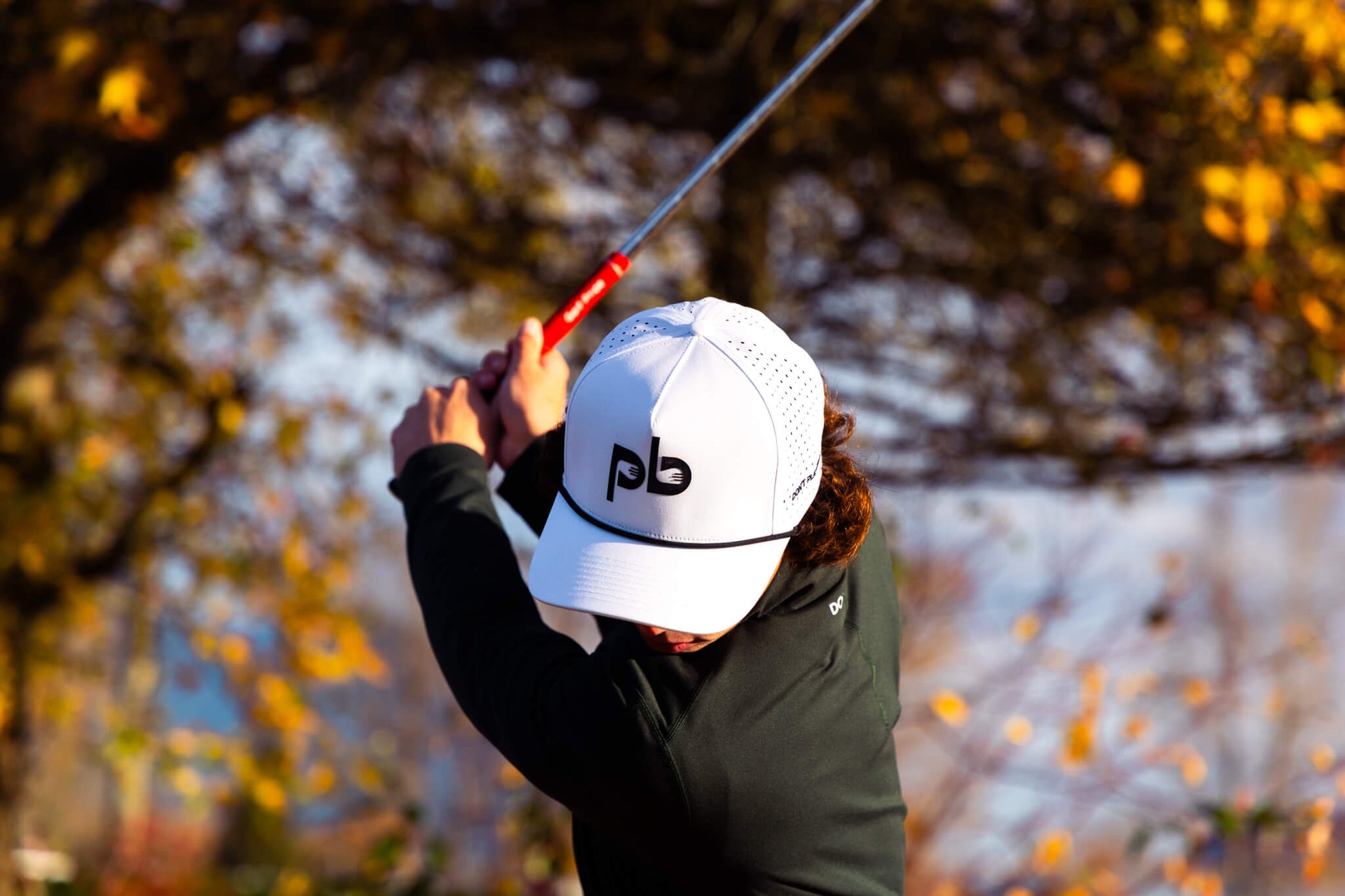 Person playing golf with a white pocket brush cap featuring a logo in an outdoor setting